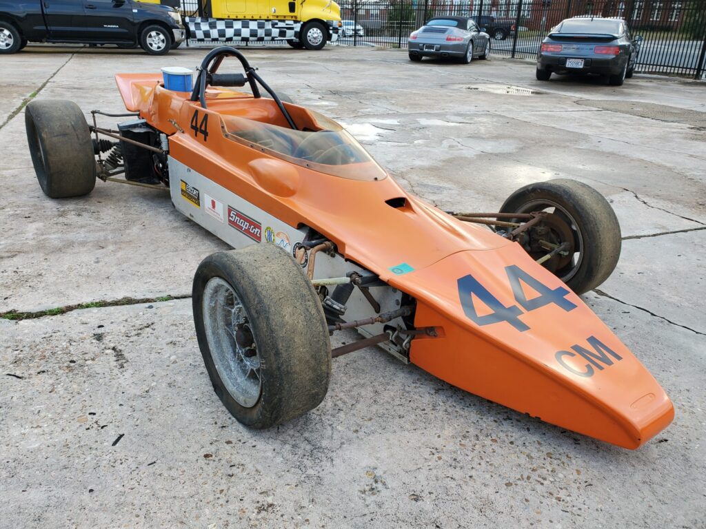 Orange vintage race car with number 44 parked outdoors.