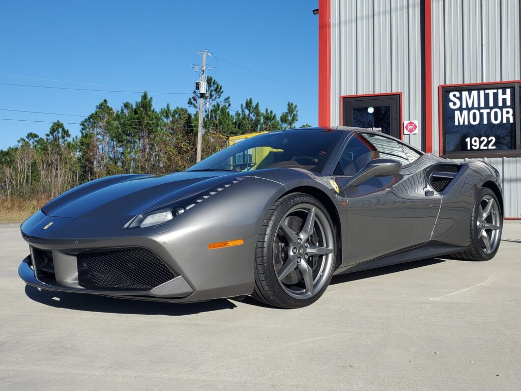 Sleek gray sports car parked on concrete near a red and white building.